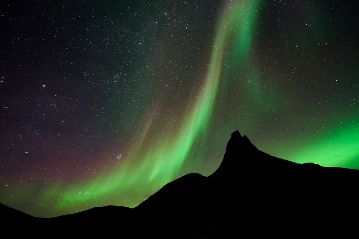 Green northern lights above a dark mountain ridge