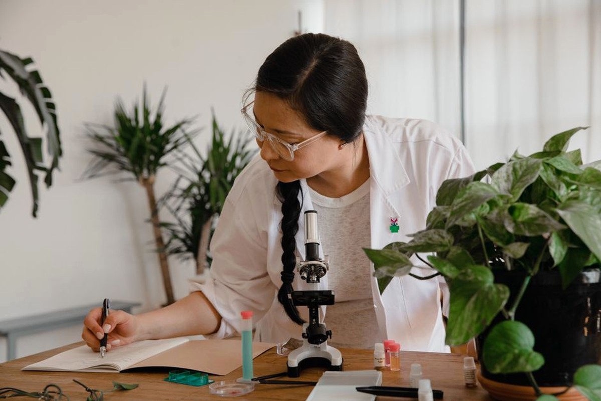 A researcher making notes beside a microscope and plants