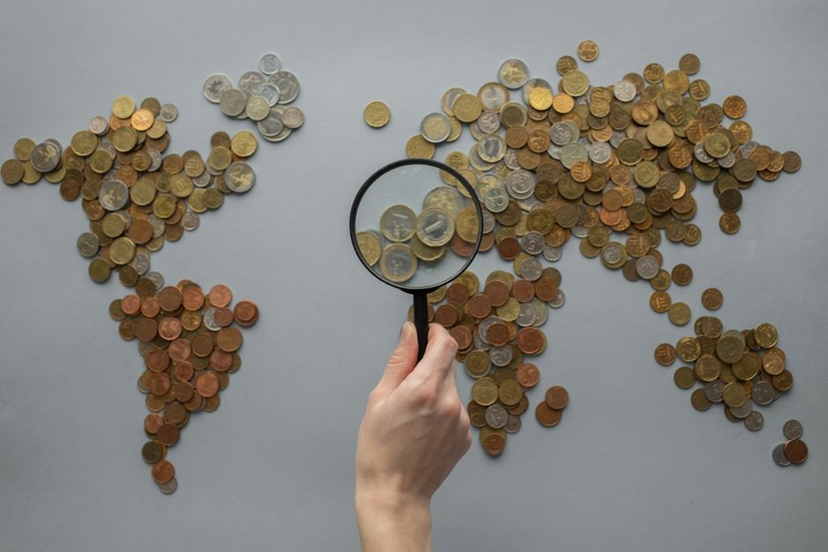 Coins arranged across a world map with a magnifying glass